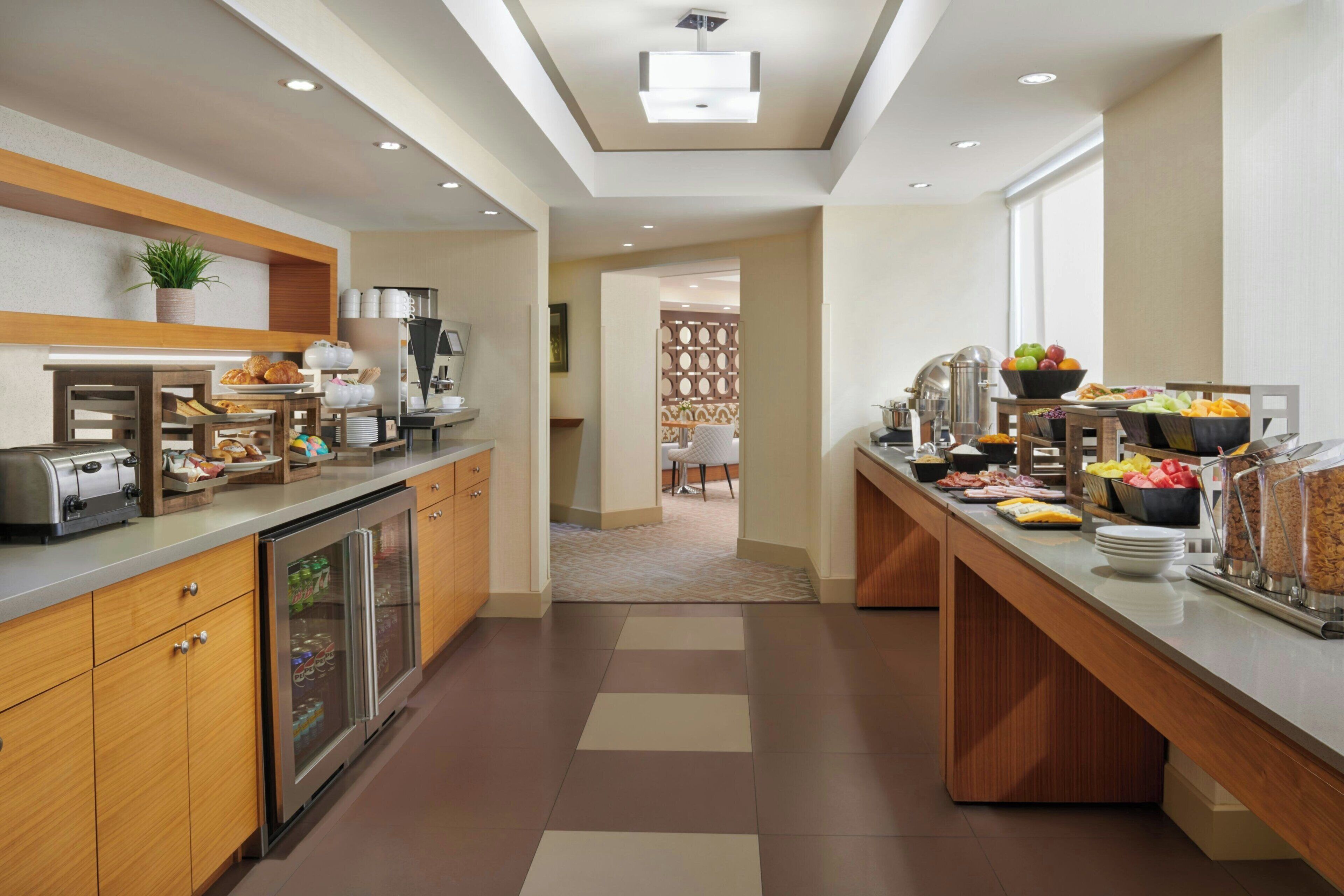 A modern hotel kitchen with a buffet setup, including a refrigerator, toaster, and various food items.