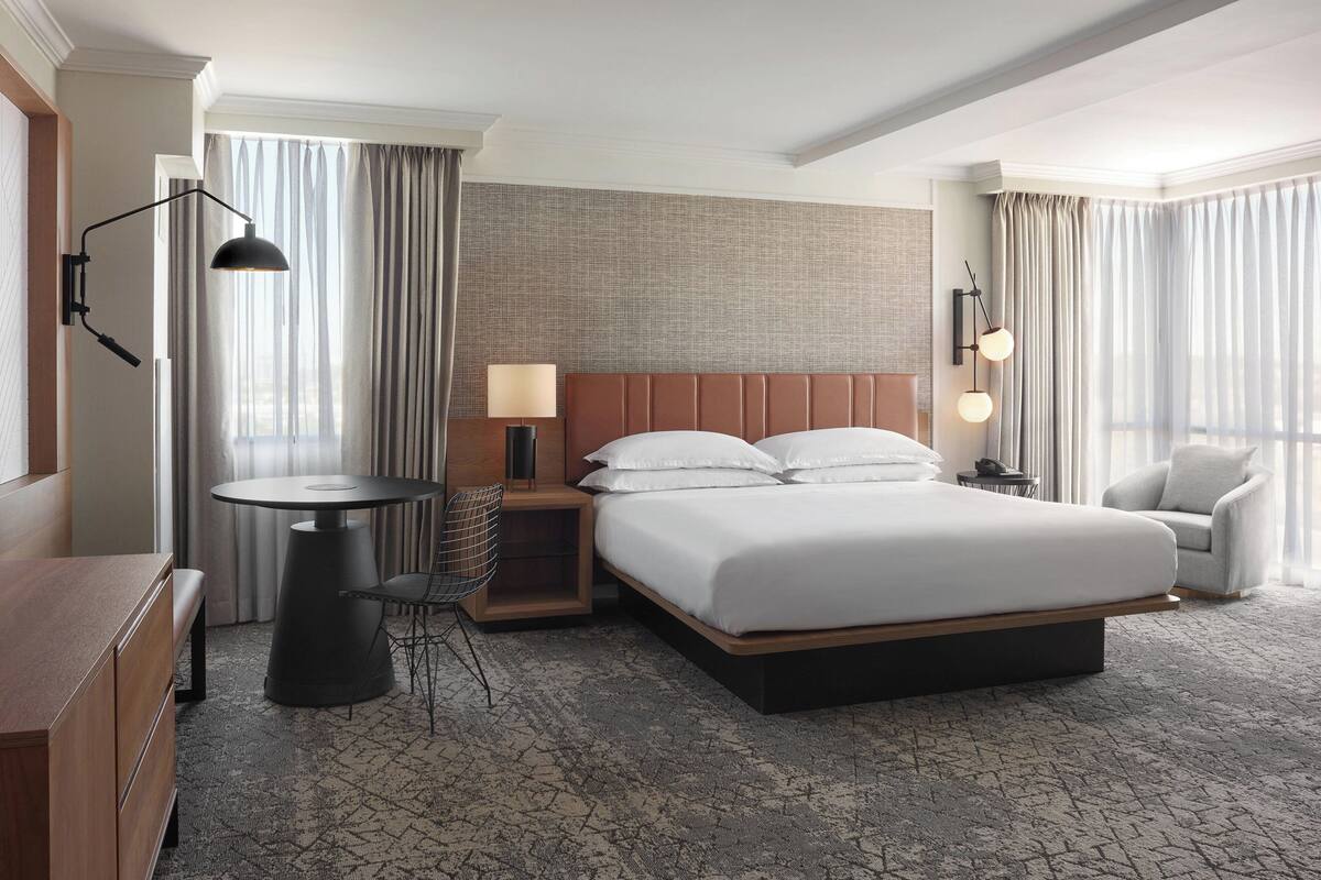 Une chambre d’hôtel avec un grand lit, un bureau avec une chaise, une petite table et une lampe.