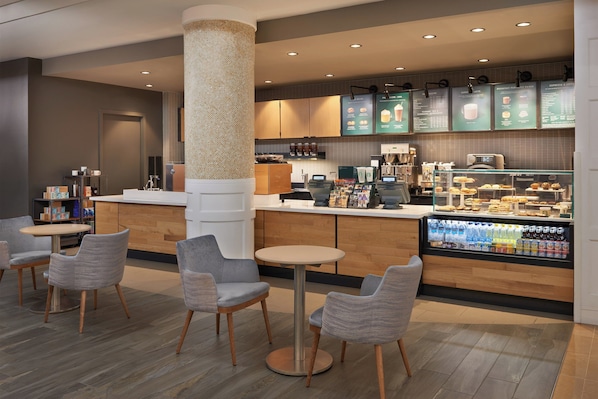 Un café moderne doté d’un comptoir central, d’un espace salon et d’une vitrine réfrigérée où sont exposées les boissons.