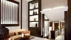 Un interior moderno con un sofá, una mesita de centro y una estatua decorativa de Buda. Hay estanterías con diversos objetos y una escalera que conduce a otro nivel.