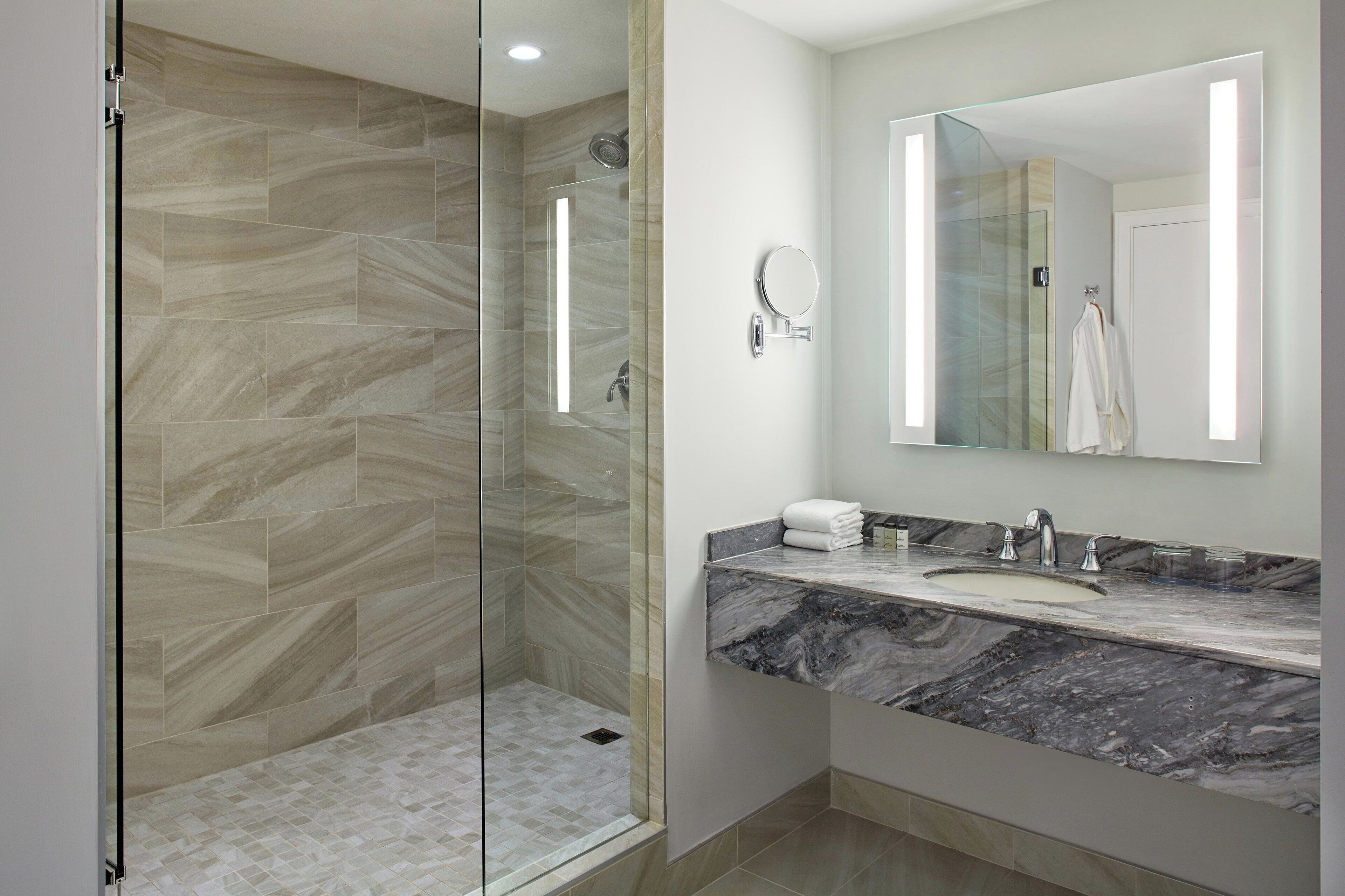 Une salle de bain moderne avec une douche à parois de verre, un lavabo en marbre et un grand miroir.