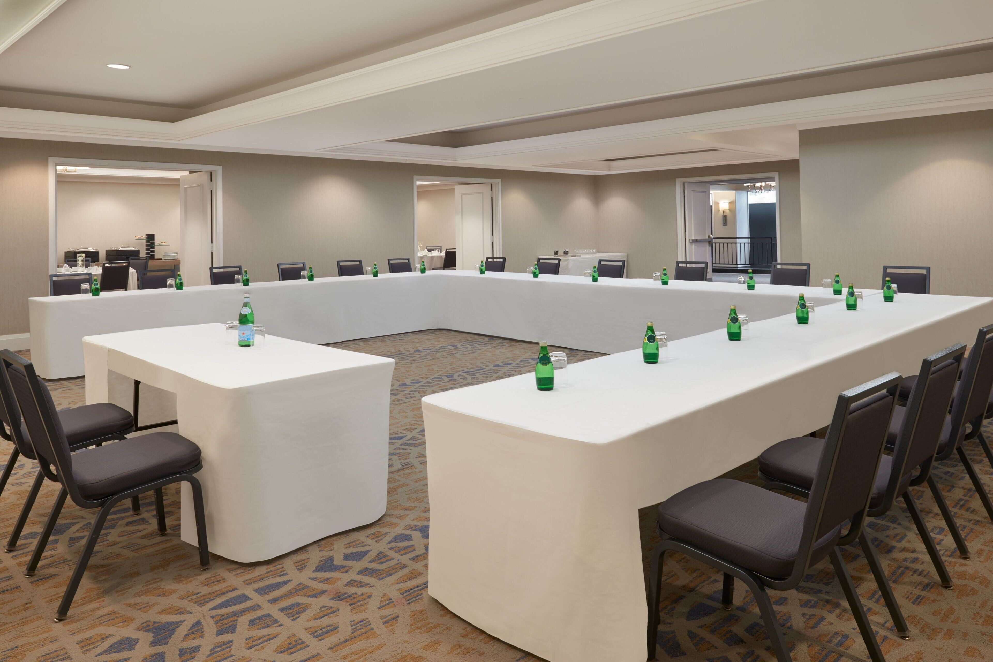 Un salón de conferencias con una larga mesa y sillas, equipado con botellas de agua y un mantel blanco.