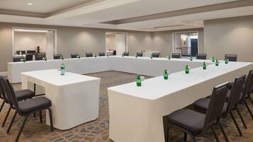 Un salón de conferencias con una larga mesa y sillas, equipado con botellas de agua y un mantel blanco.