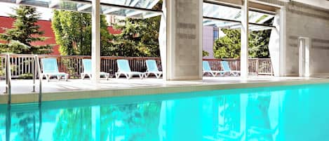 A swimming pool with sun loungers and a view of trees and buildings.