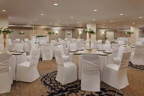 A banquet hall with round tables set for dining, white chairs, and floral centerpieces.