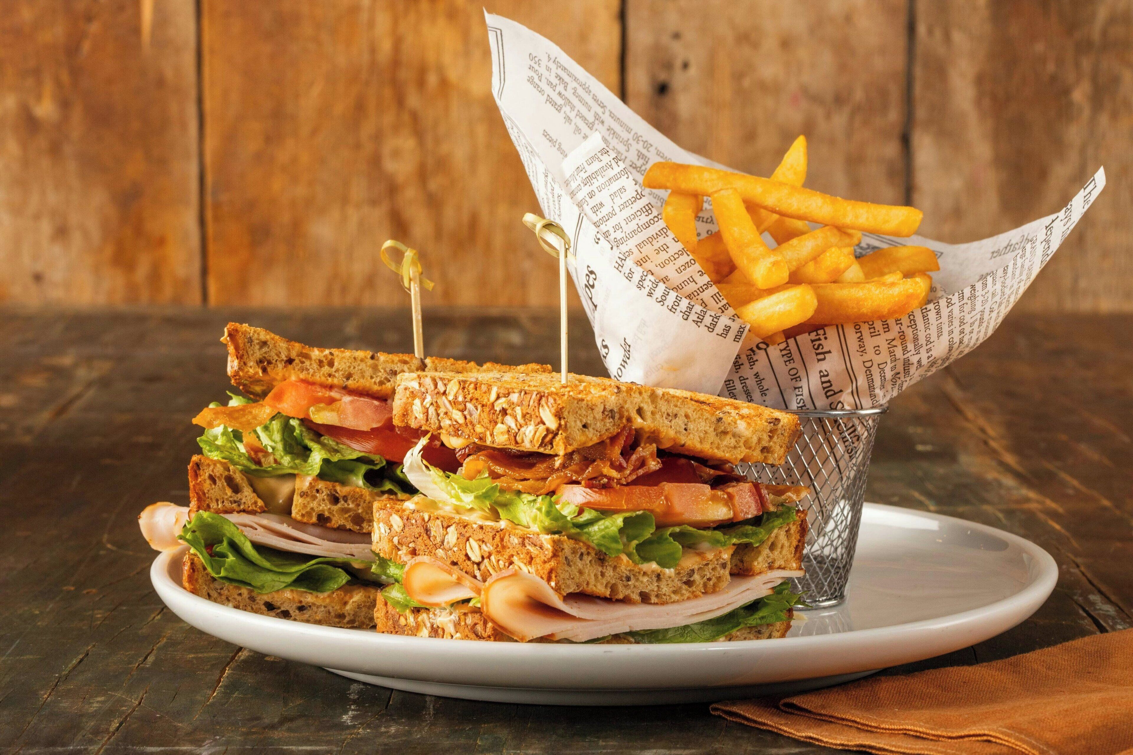 Ein Sandwich mit Zahnstocher, ein Teller und eine Korb mit Pommes.