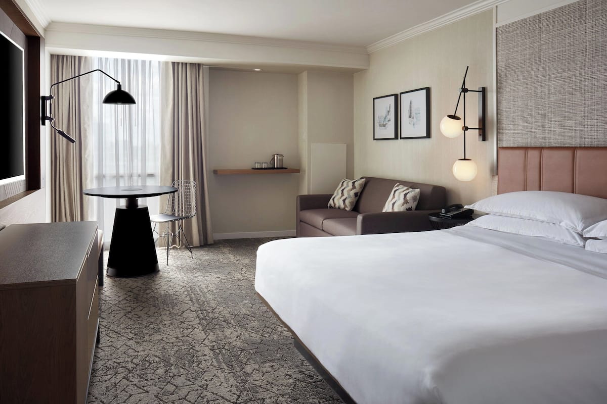 Une chambre d’hôtel avec un grand lit, un bureau avec une chaise, une petite table, un canapé et un téléviseur.