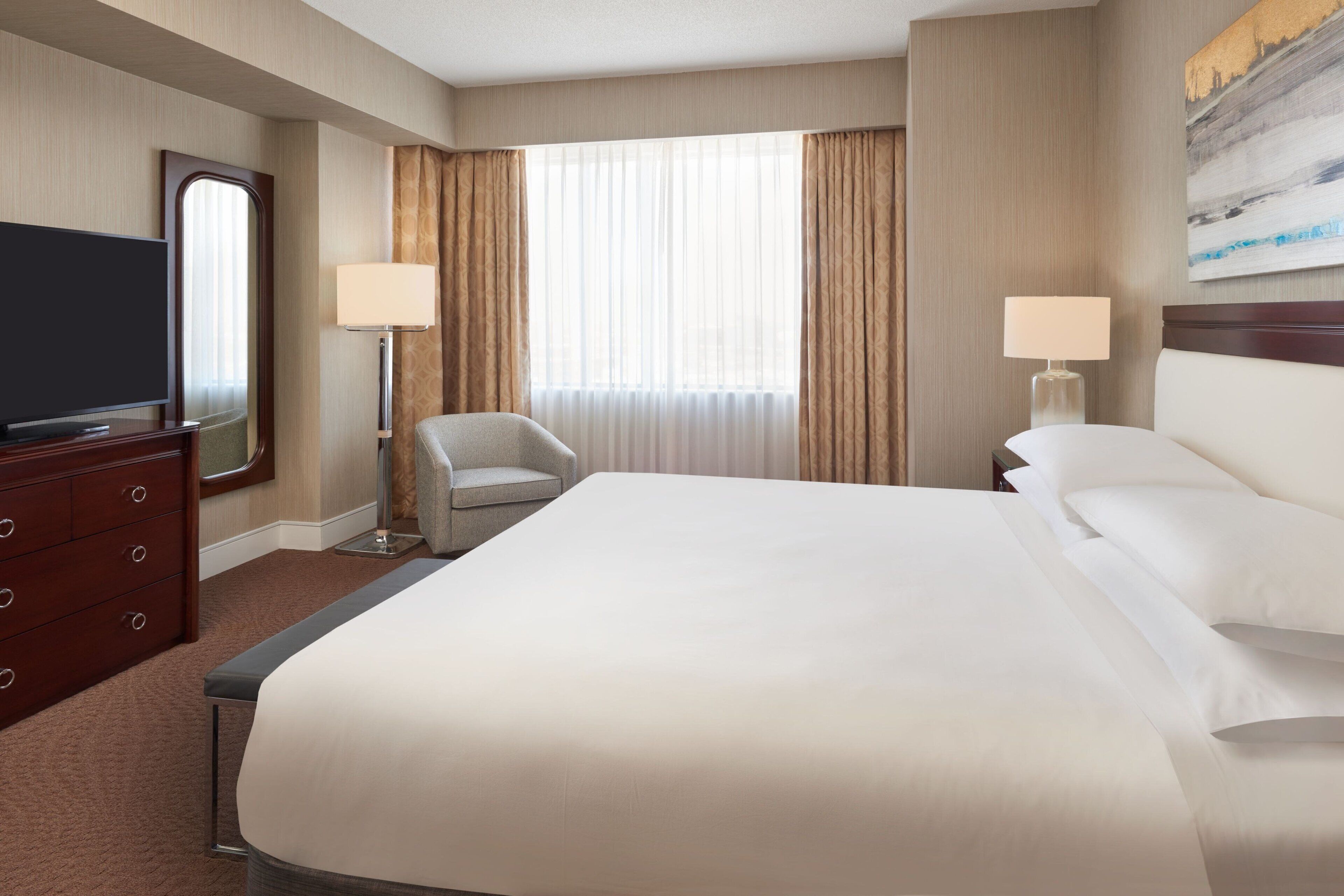 A hotel room with a large bed, a TV, a chair, and two lamps.