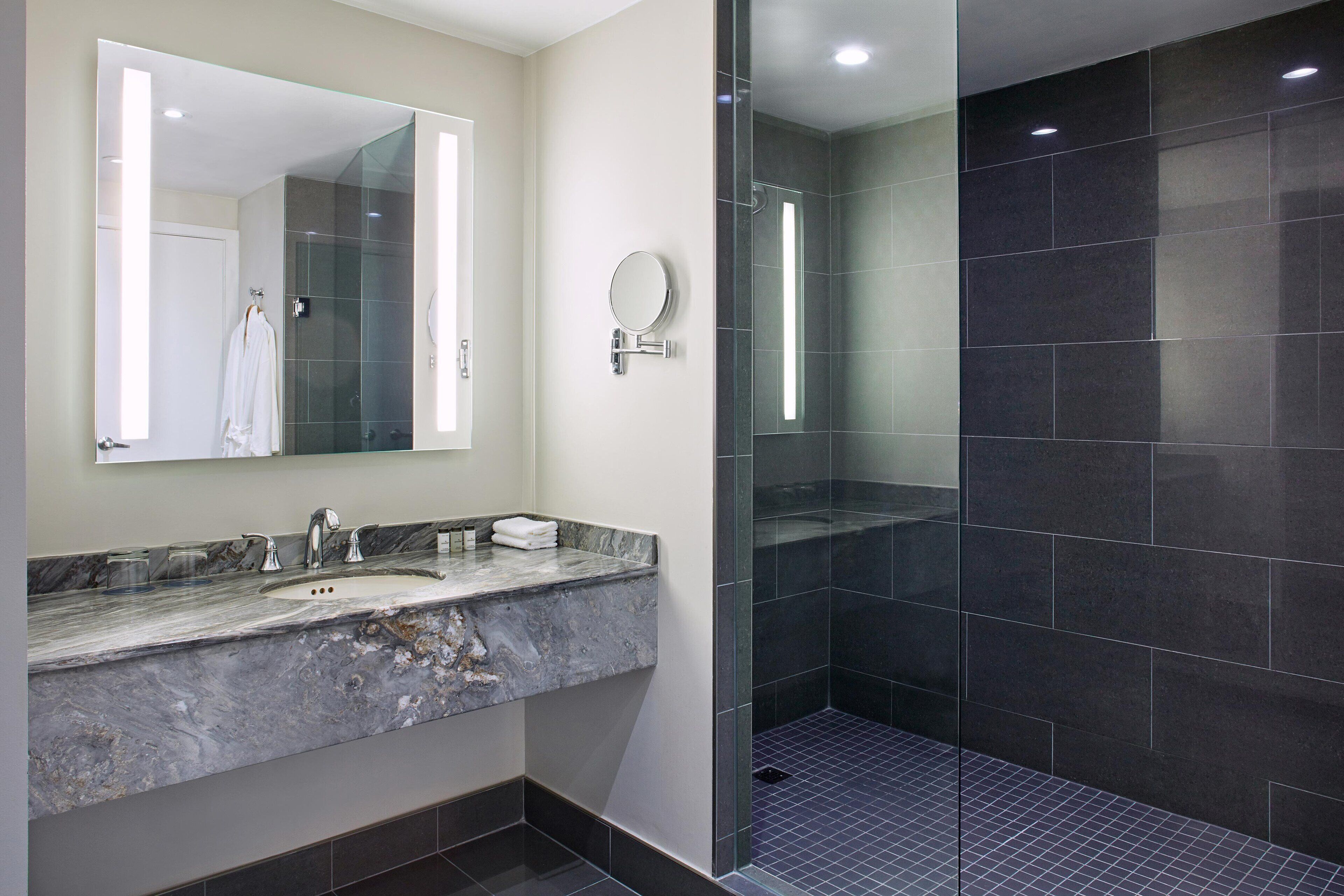 Une salle de bain moderne avec un lavabo en marbre, un grand miroir et une douche séparée par une paroi de verre.