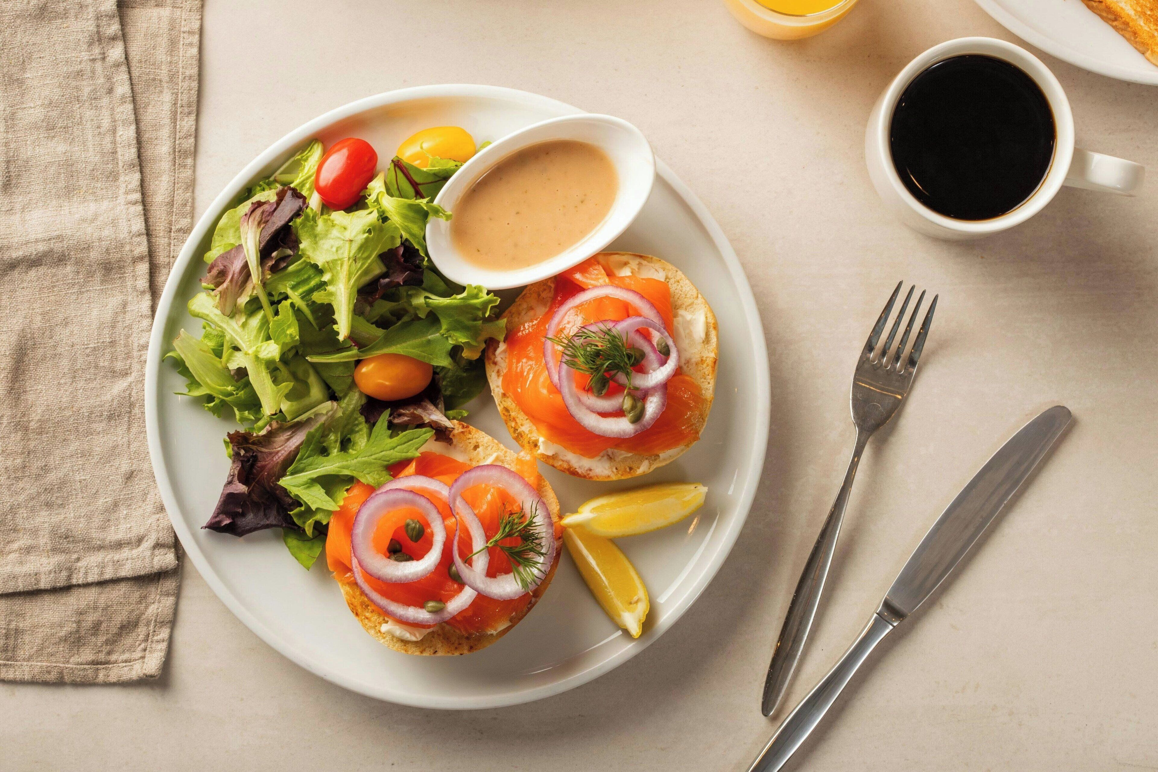 A plate with two open-faced sandwiches, a side salad, lemon wedges, and a small bowl of sauce.