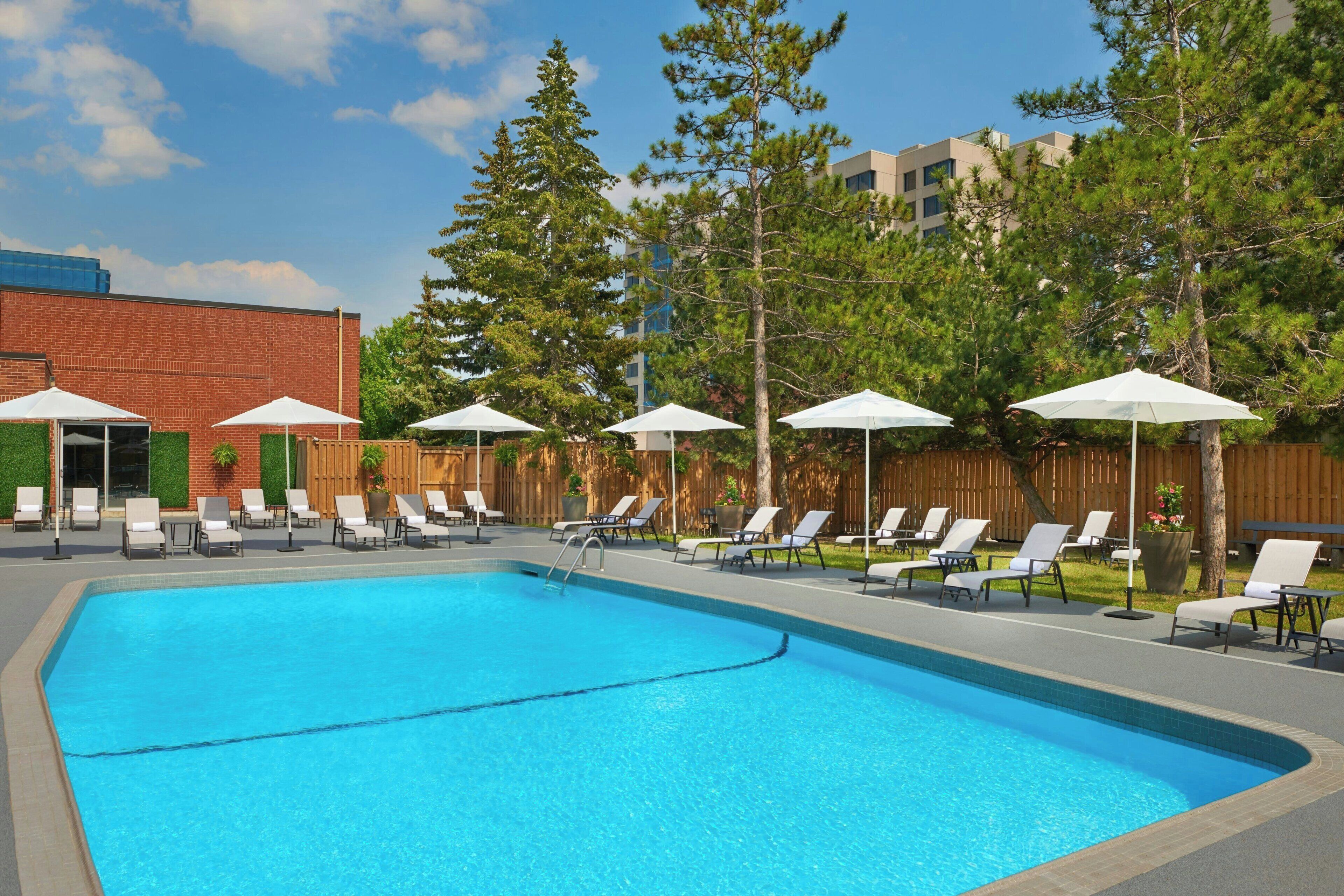 A swimming pool with lounge chairs and umbrellas, surrounded by trees and a building.