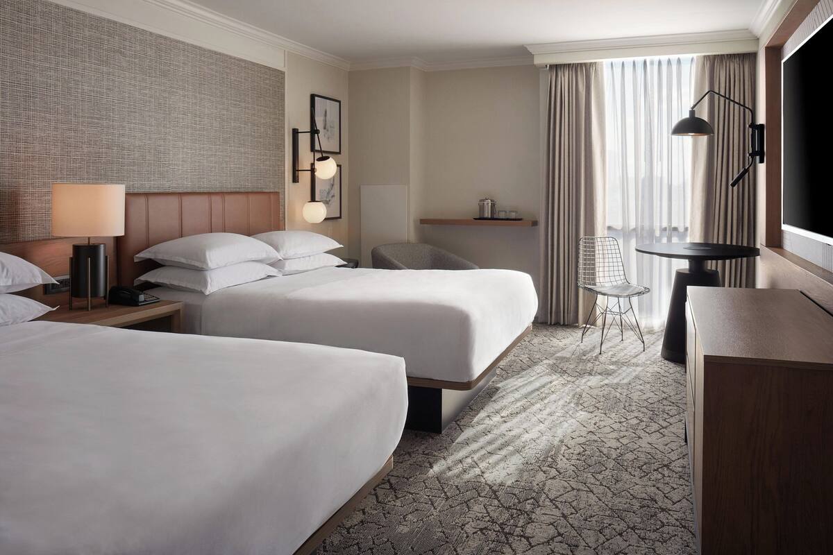 Une chambre d’hôtel avec deux lits, un bureau, une chaise, une télévision et une fenêtre avec des rideaux.