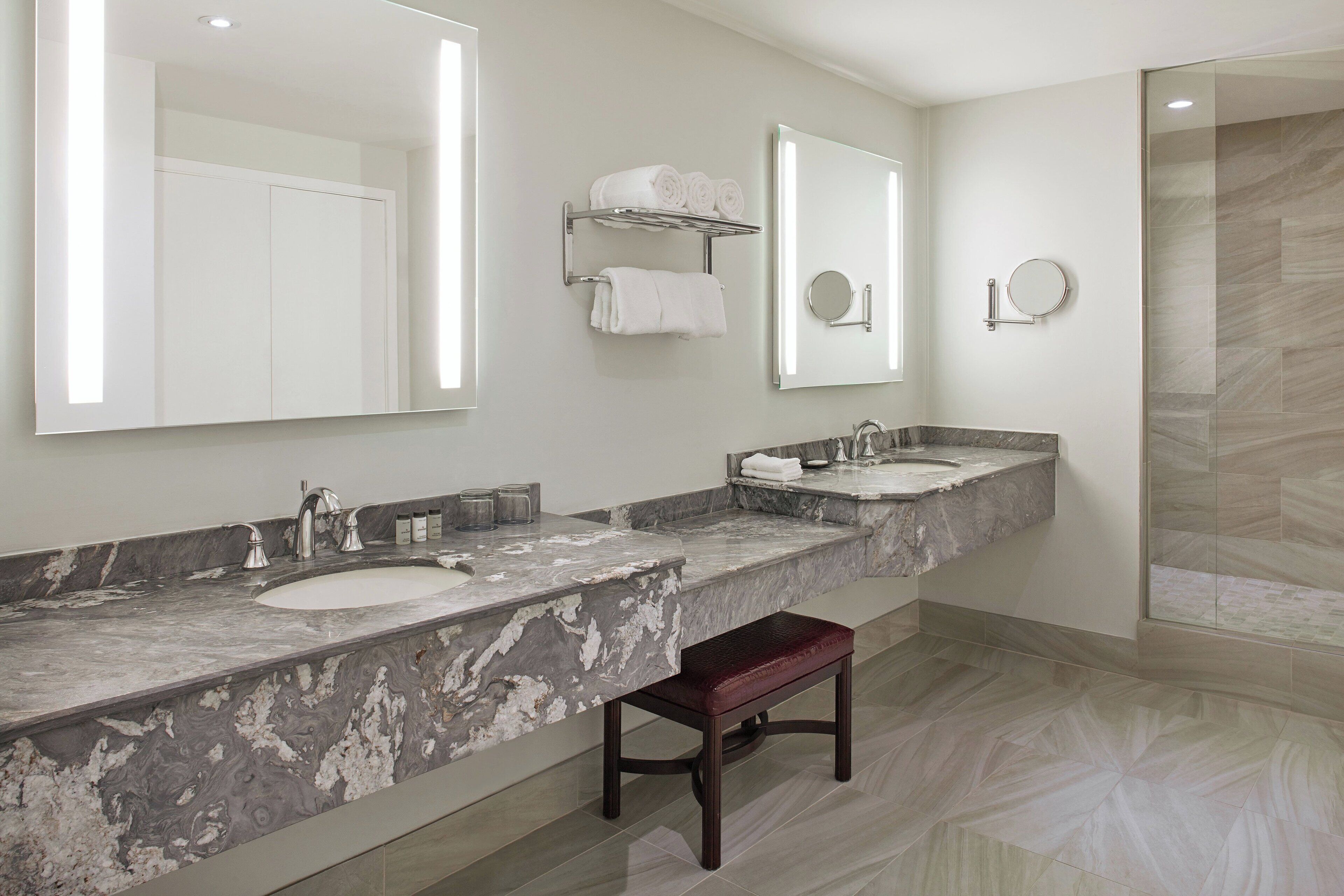 A modern bathroom with two sinks, a large mirror, and a bench.