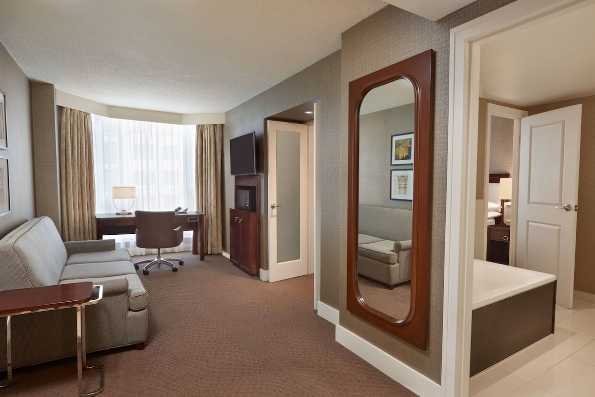Une chambre d’hôtel équipée d’un canapé, d’un bureau, d’une chaise, d’une télévision et d’un grand miroir.