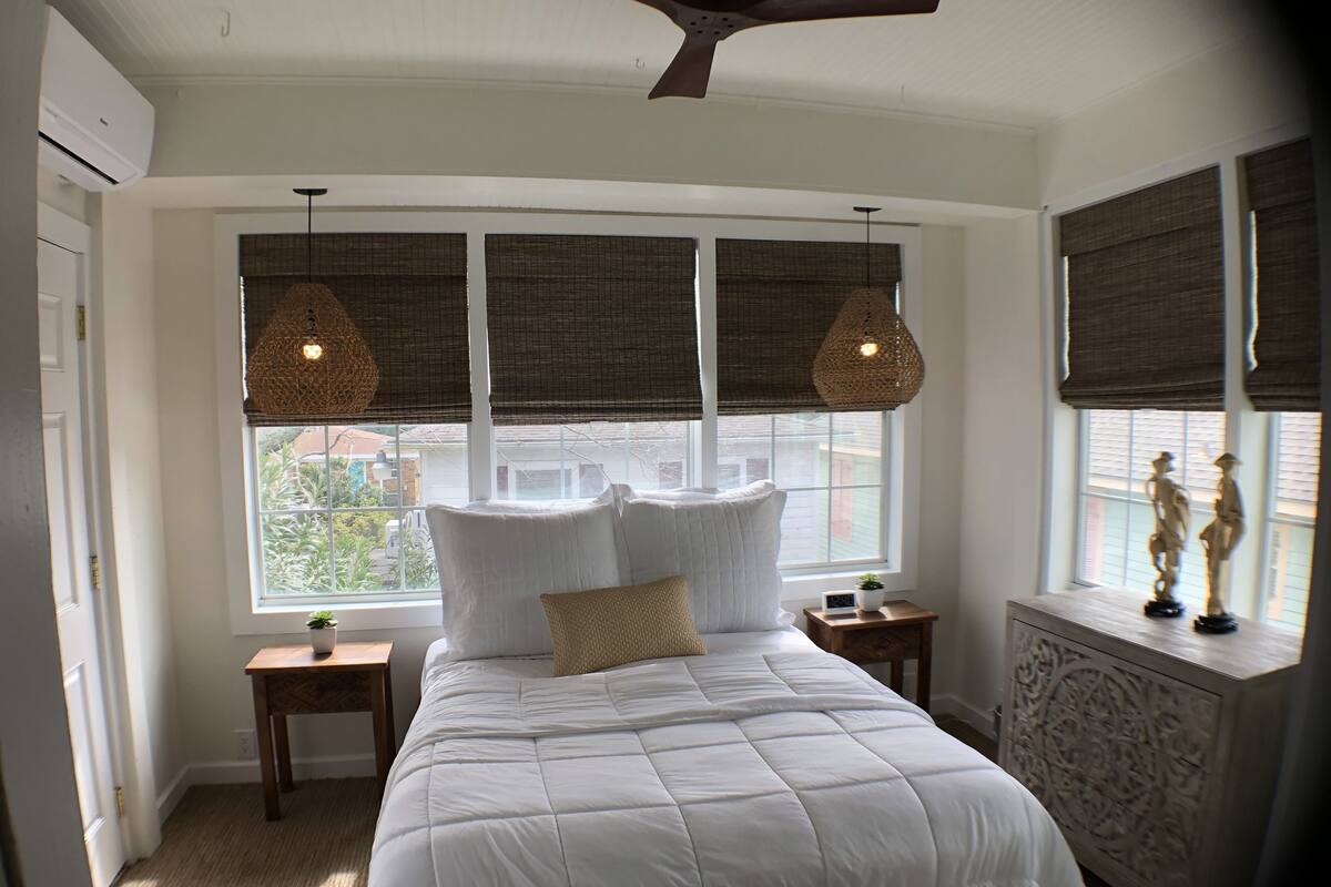 A bedroom with a large bed, two bedside tables, a ceiling fan, and a window with blinds.