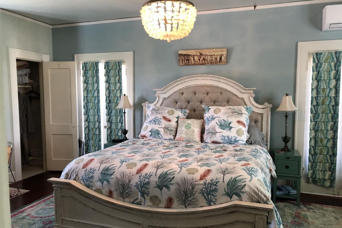 A bedroom with a bed, a chandelier, a framed picture on the wall, and curtains.