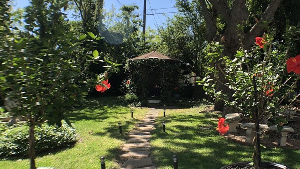 A garden pathway leading to a gazebo surrounded by potted plants and trees.