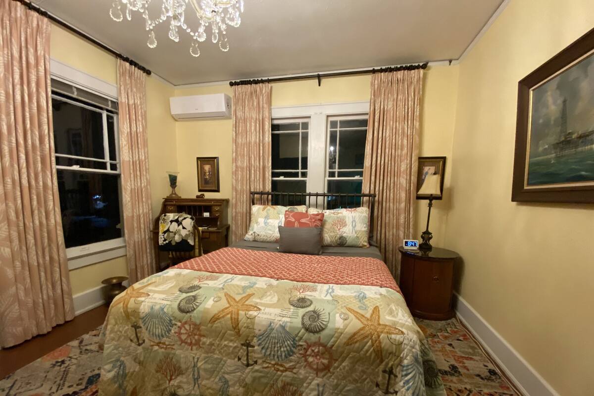A bedroom with a bed, curtains, a chandelier, a clock, and a painting on the wall.
