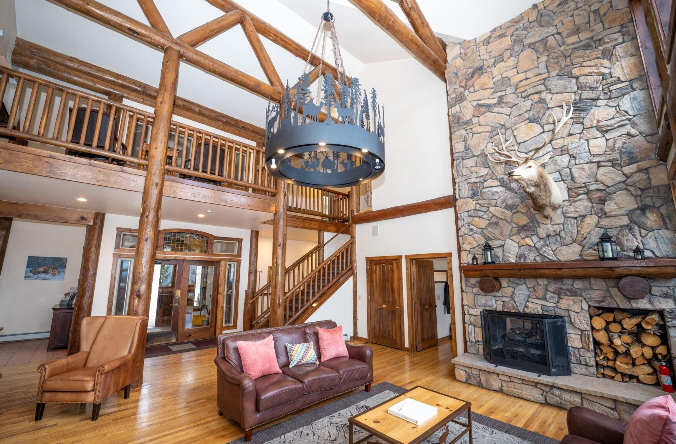 A spacious interior with a high ceiling, a stone fireplace, a leather sofa, and a chandelier.