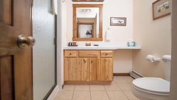 A bathroom with wooden cabinets, a white toilet, a mirror with lights, and a framed picture on the wall.