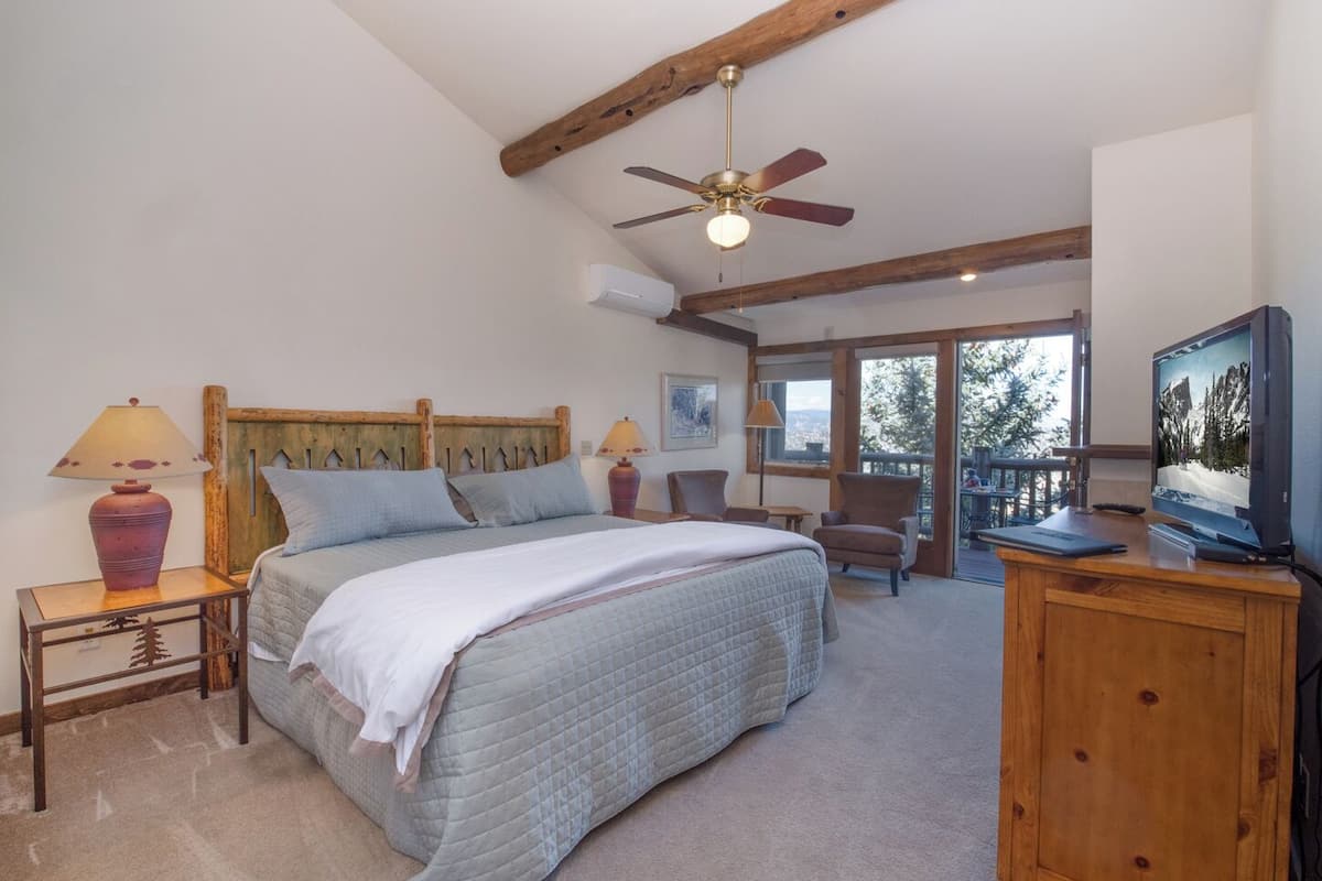 A bedroom with a bed, a ceiling fan, a TV, and a view of the outdoors.