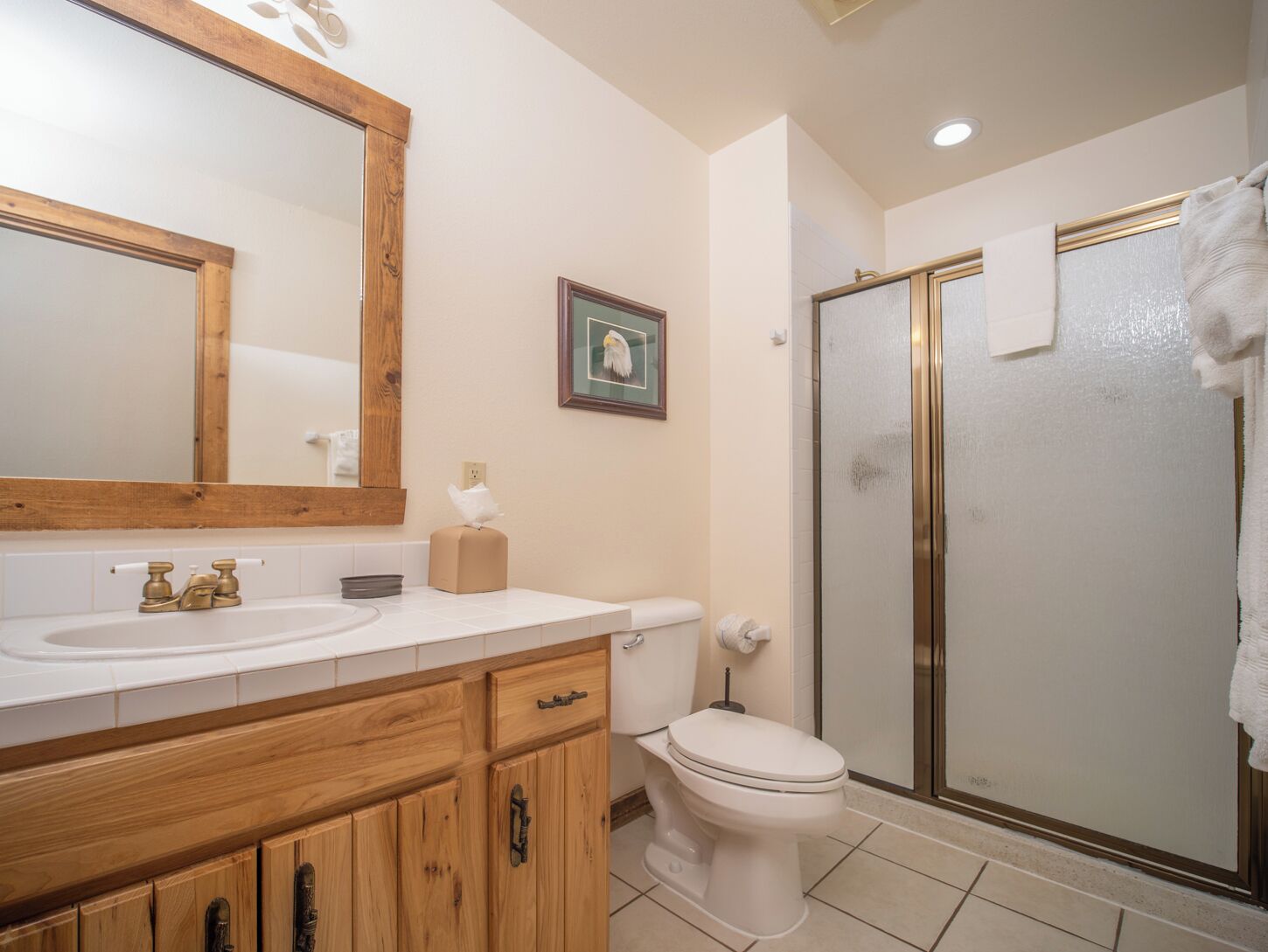 Une salle de bain avec un meuble-lavabo en bois, des toilettes, une douche avec des portes en verre et un tableau encadré au mur.