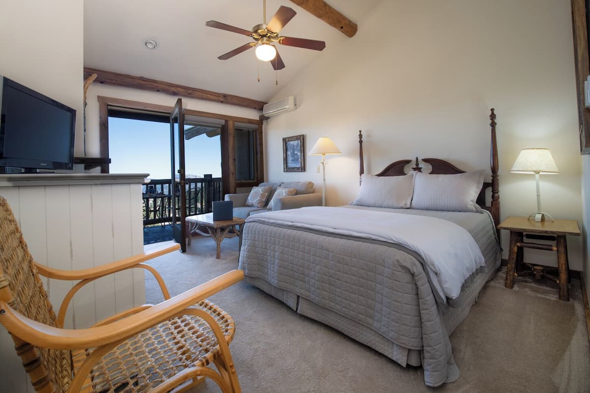 A bedroom with a bed, a chair, a desk, a television, and a balcony with a view.