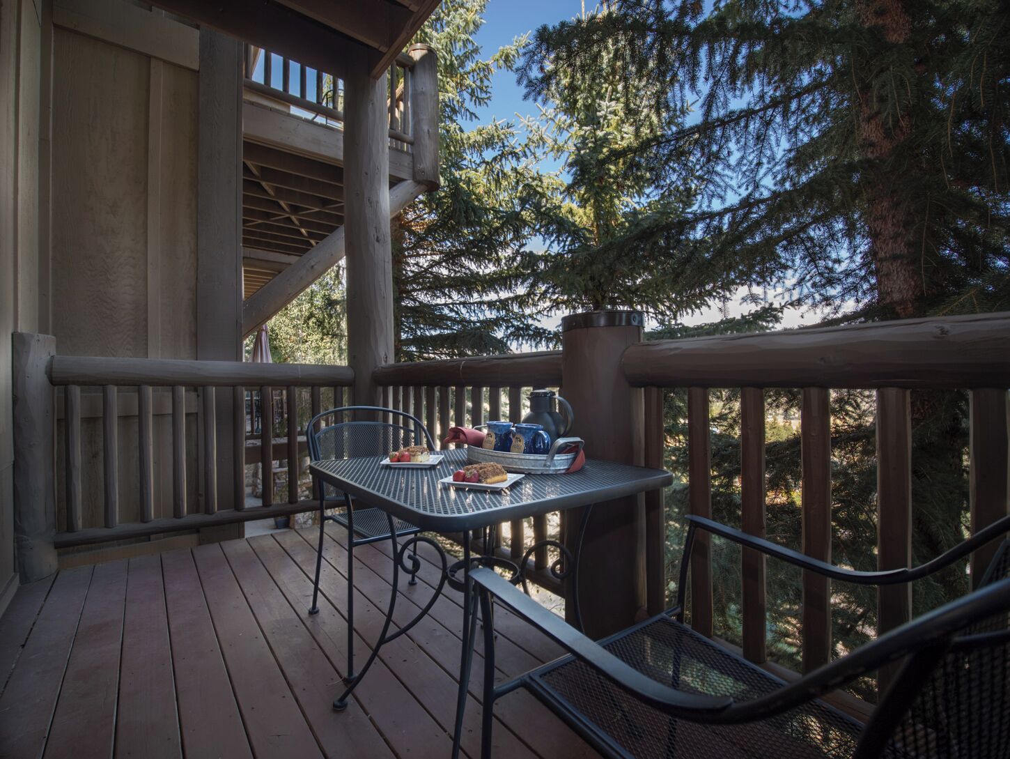A wooden deck with a metal table and chairs, a kettle, and a tray with food.