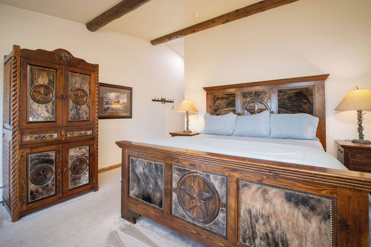 A bedroom with a wooden bed, two bedside tables, a wooden wardrobe, and a ceiling with exposed beams.