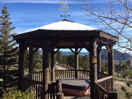 Un gazebo in legno con un tetto imbiancato dalla neve, circondato da alberi e montagne.