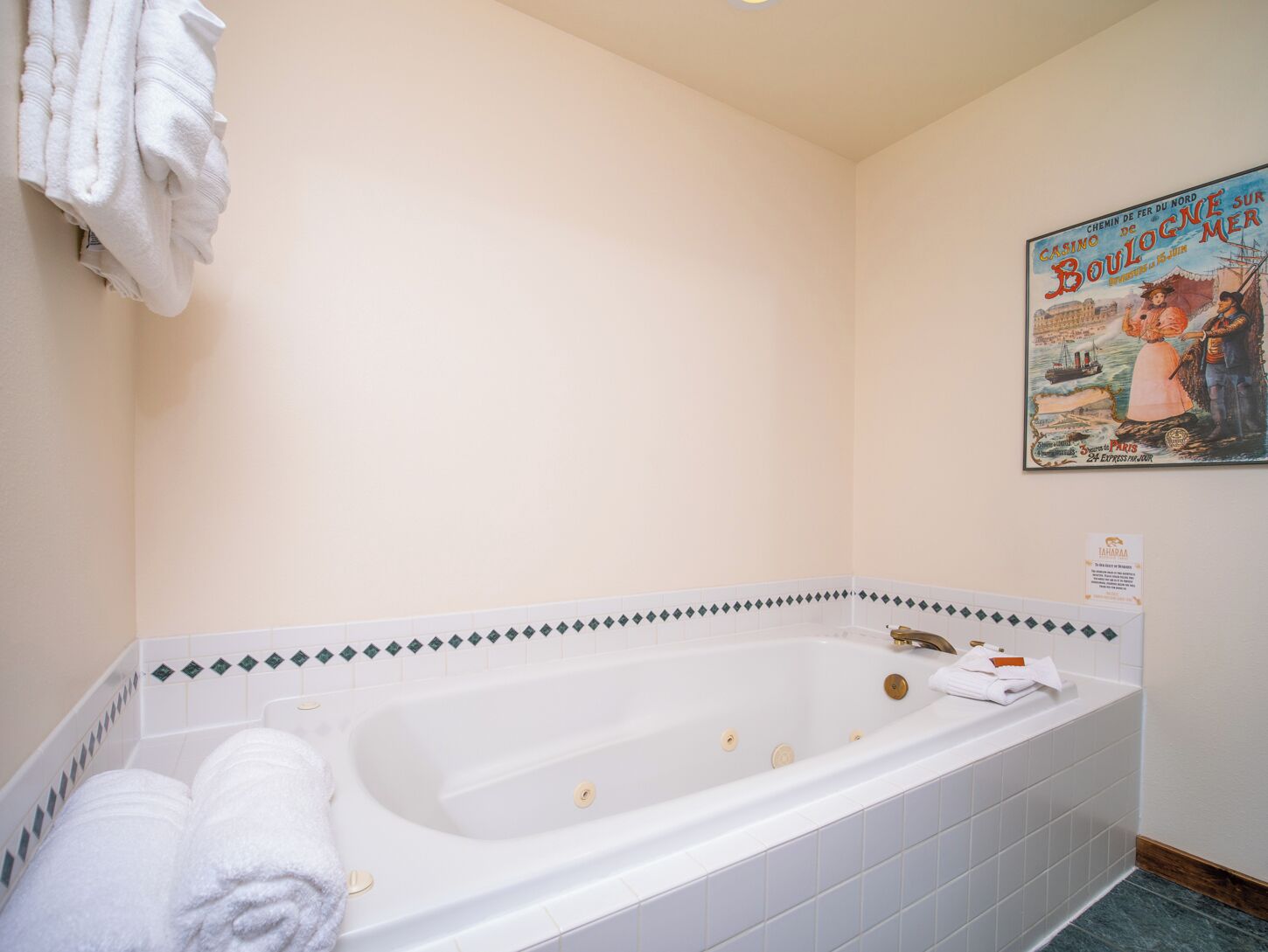 A bathroom with a large bathtub, white towels, and a vintage poster on the wall.