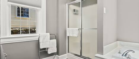 A bathroom with a glass shower enclosure, a white sink, and a window with a towel rack.