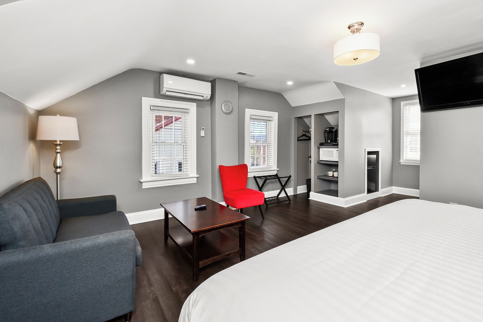 A bedroom with a bed, a red chair, a small table, a lamp, and a TV.