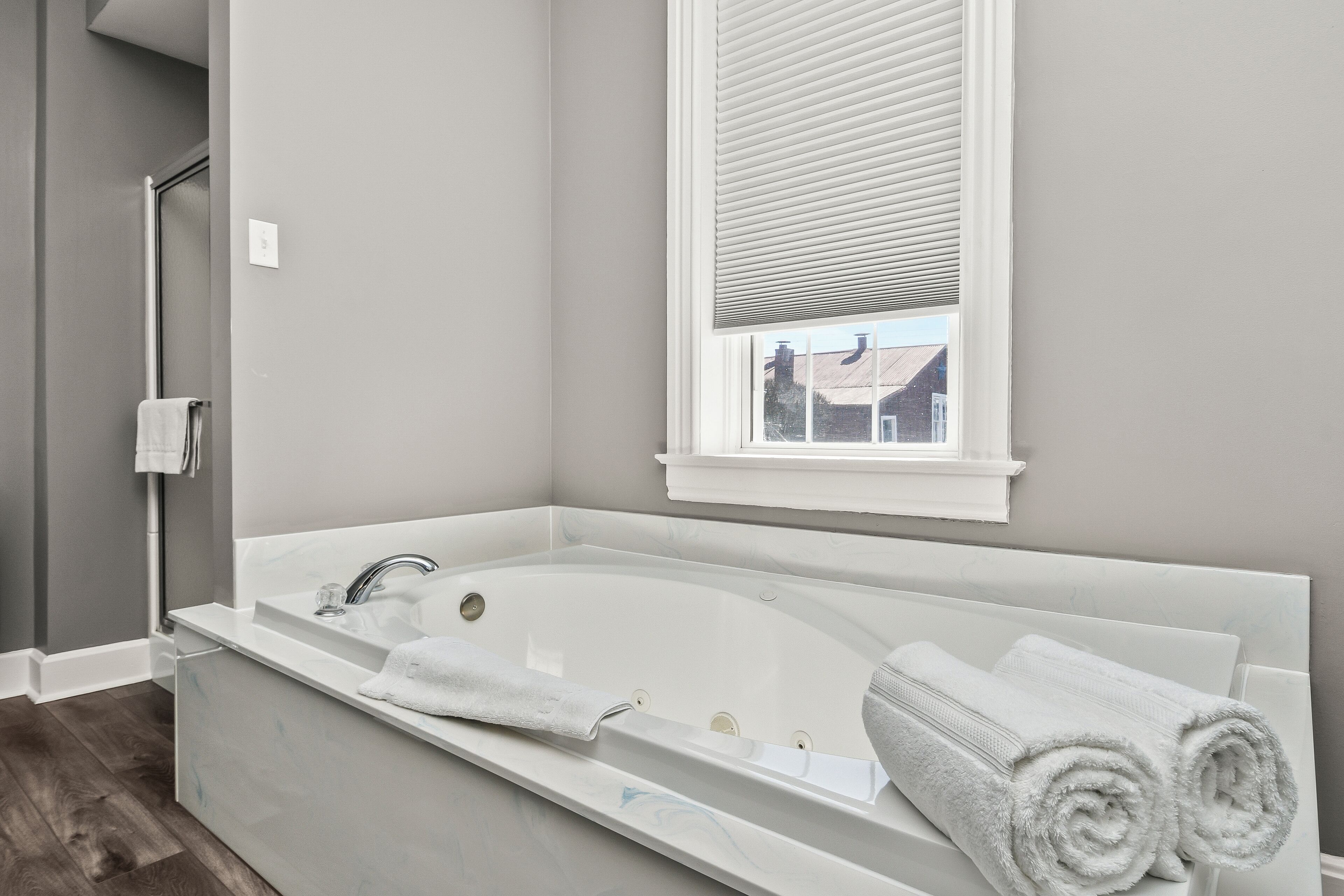 A modern bathroom with a large bathtub, a window with blinds, and a towel rack.