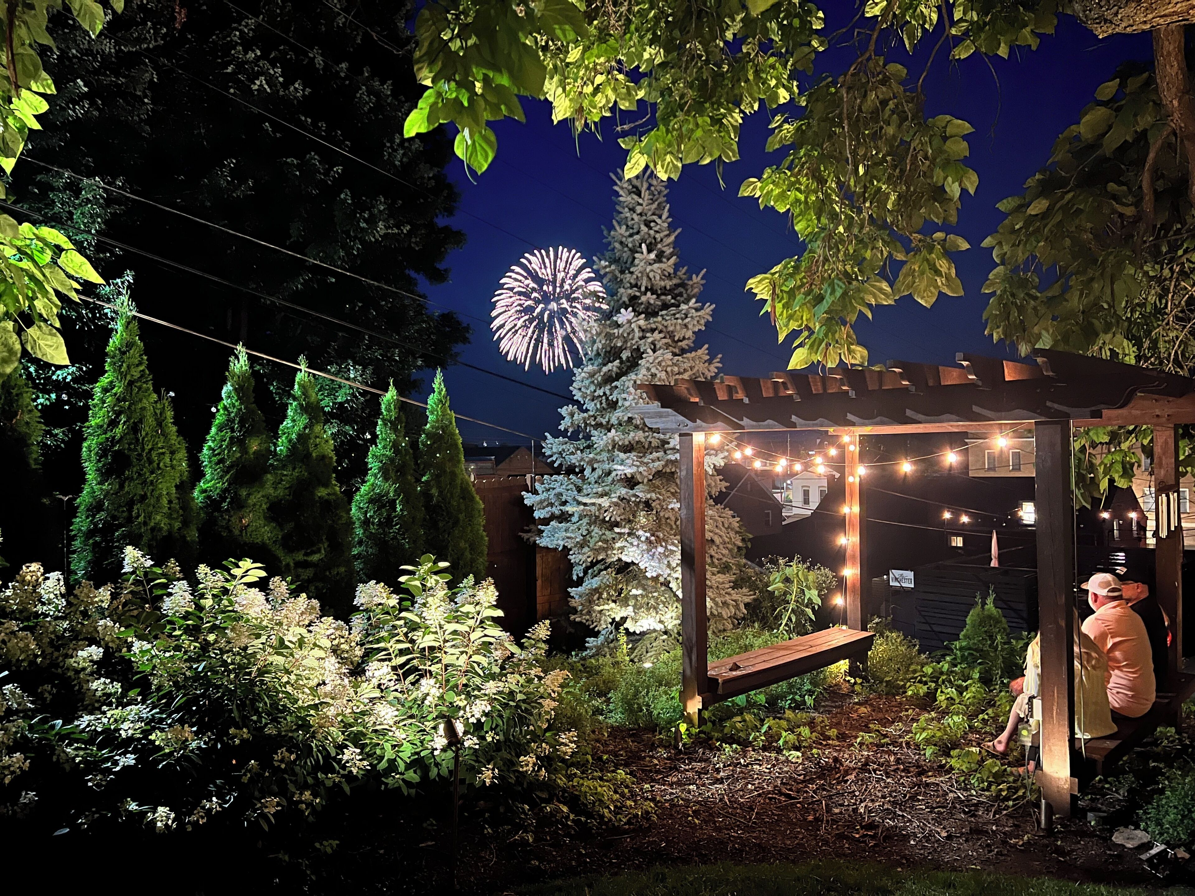A garden with a wooden pergola, string lights, and a bench.