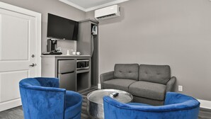 Un espacio habitable compacto con kitchenette, un sofá gris y dos sillones azules.