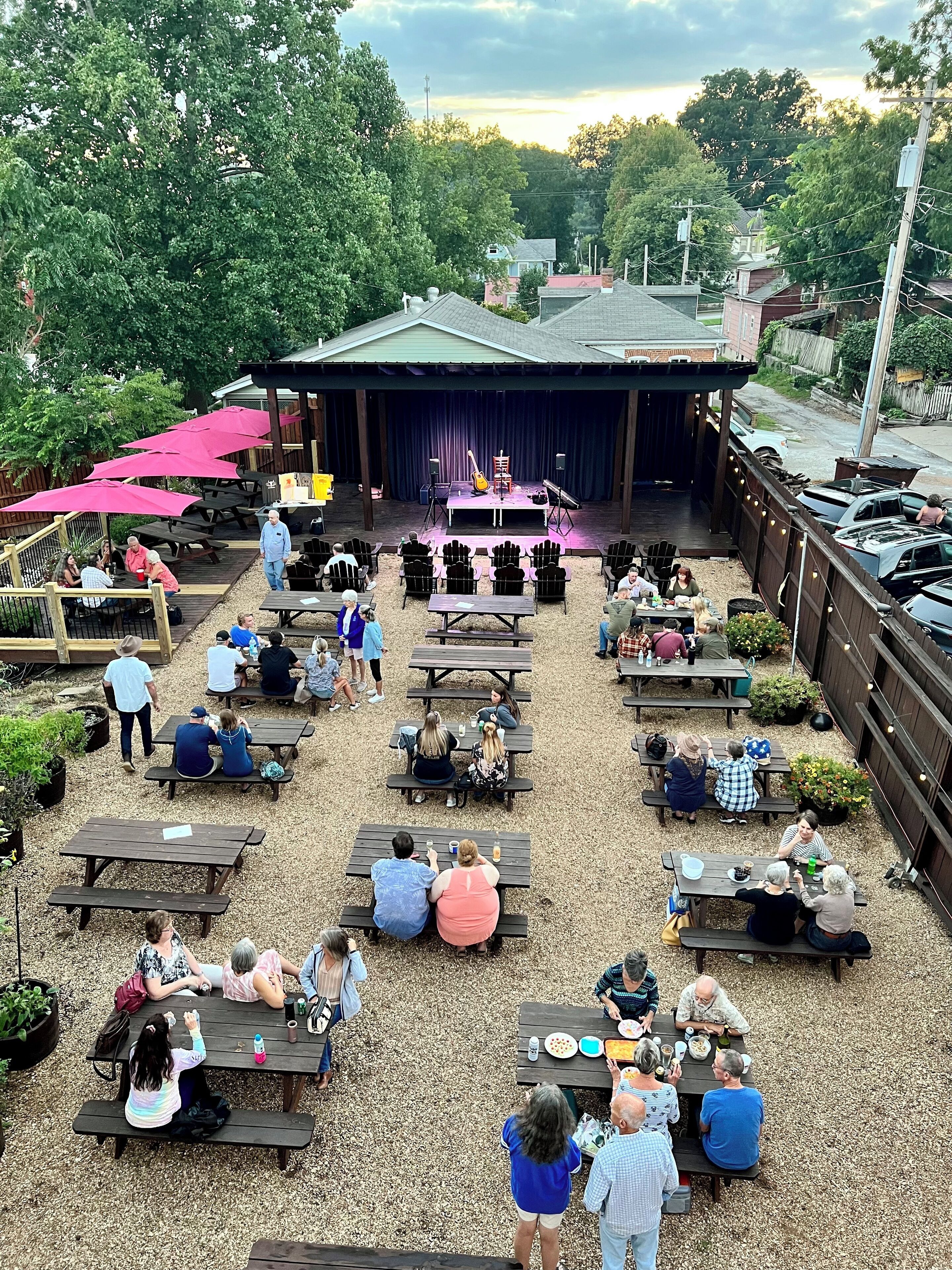 An outdoor seating area with multiple tables and chairs, a stage with musical instruments, and a covered performance area.