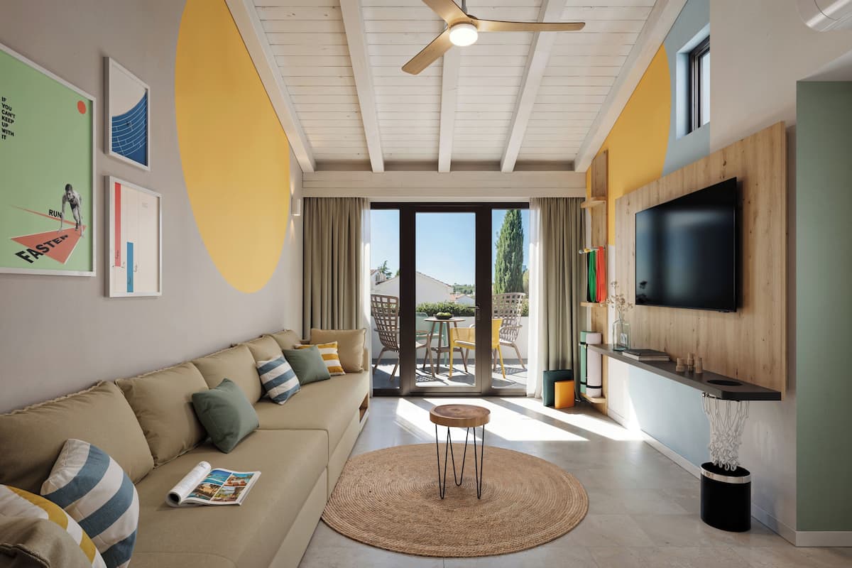 A modern living room with a sofa, a round table, a ceiling fan, and a TV mounted on the wall.