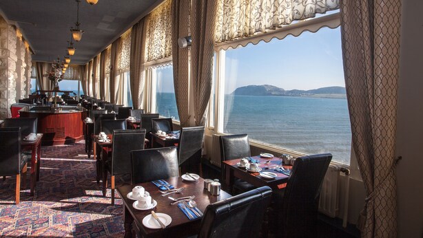 Een restaurant met eettafels, een bar en grote ramen met uitzicht op zee.