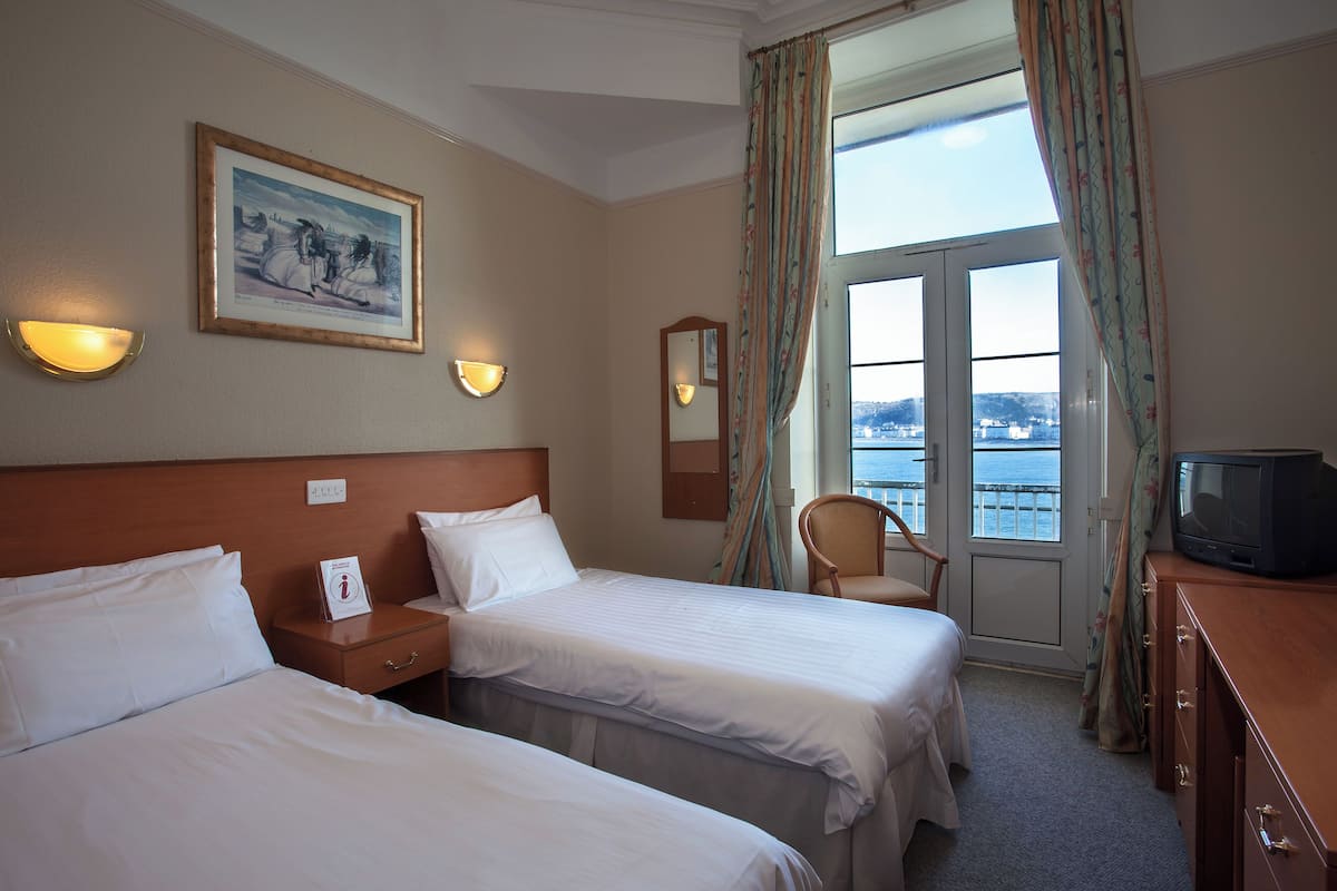 Une chambre d’hôtel avec deux lits, une télévision, un tableau au mur et une vue sur la mer par la fenêtre.