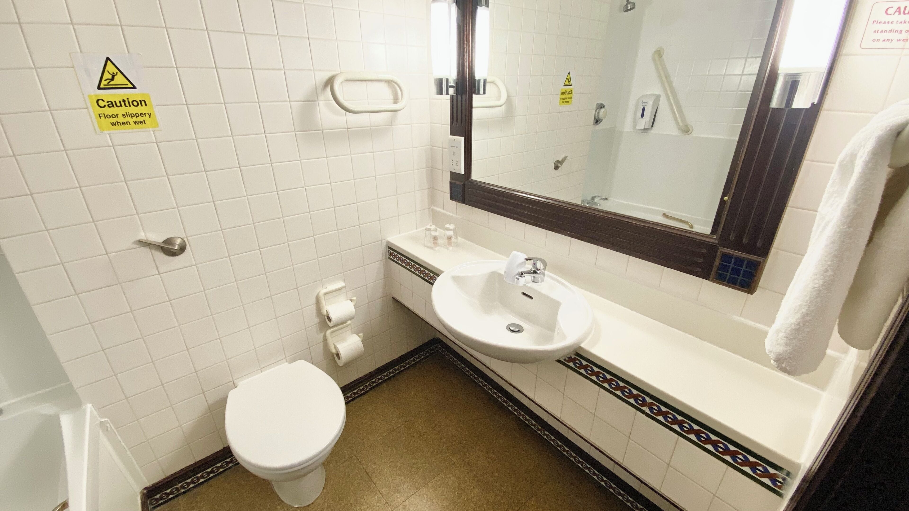 A small bathroom with a toilet, sink, and mirror. There is a caution sign on the wall and a towel hanging on the wall.