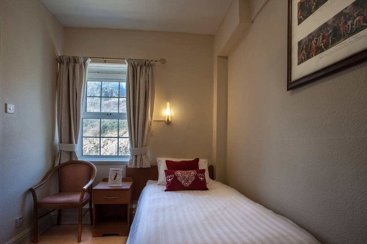 Une chambre d’hôtel avec un lit, une chaise, un bureau et une fenêtre avec des rideaux.