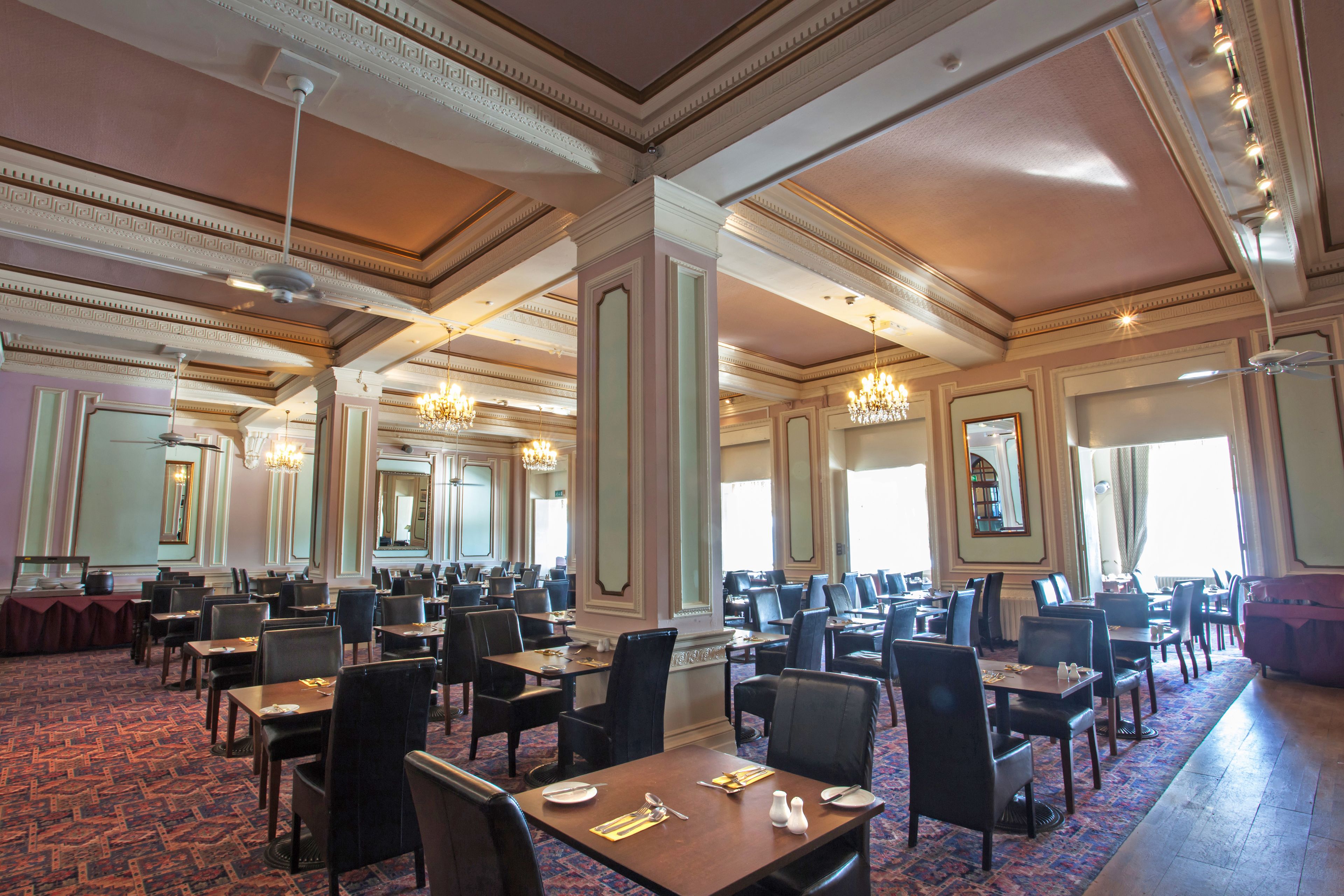 A spacious banquet hall with high ceilings, ornate moldings, and chandeliers. Tables are set with fine china and silverware.