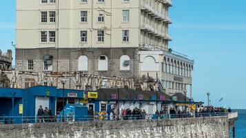 A large hotel with multiple floors and balconies, located near a waterfront with a rocky shore.