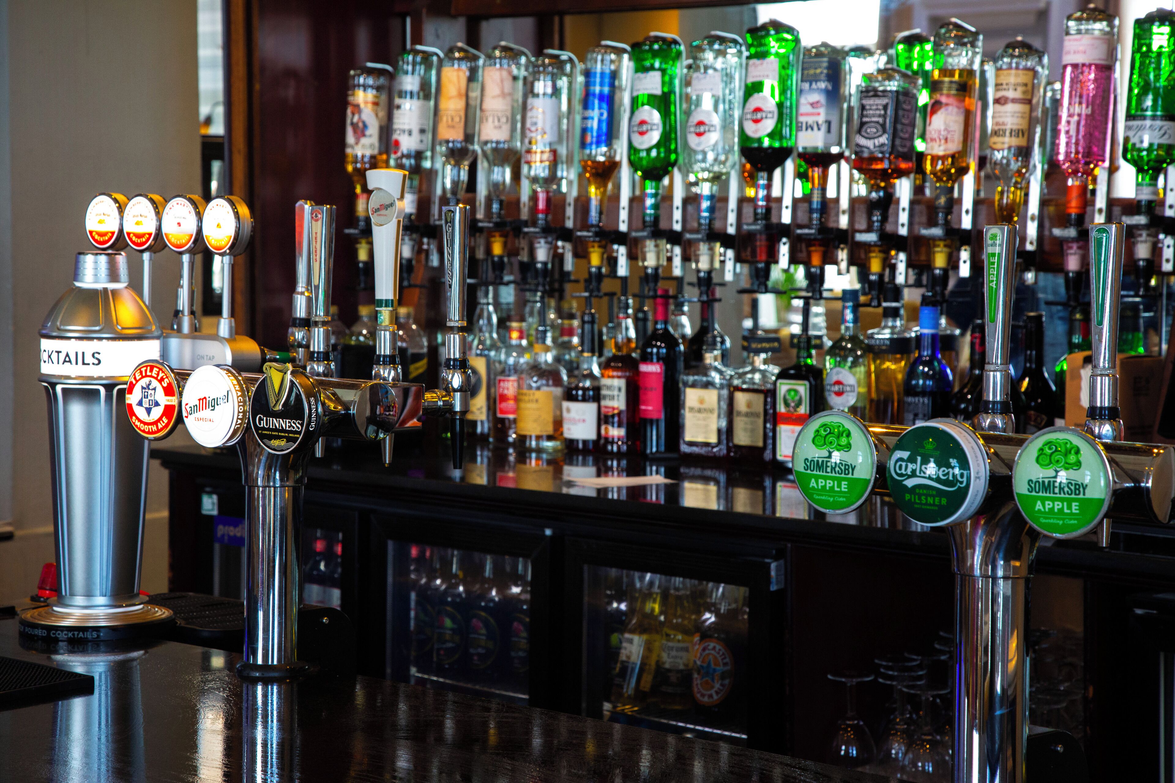 Un bar doté de nombreux robinets pour servir différents types de boissons alcoolisées, notamment des marques comme Guinness et Carlsberg, et une variété de bouteilles exposées en arrière-plan.