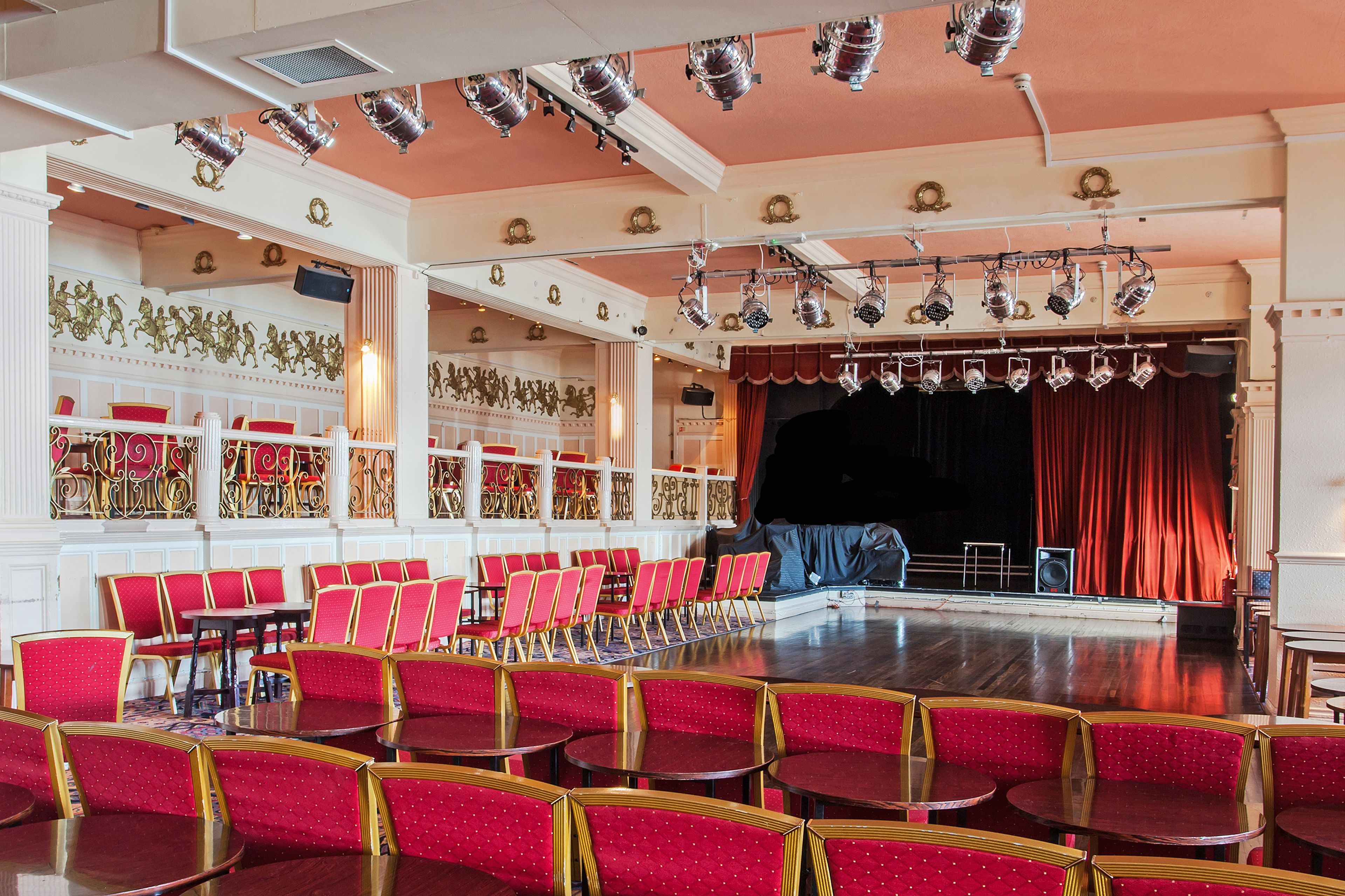 A theater with rows of red chairs and a stage with red curtains.