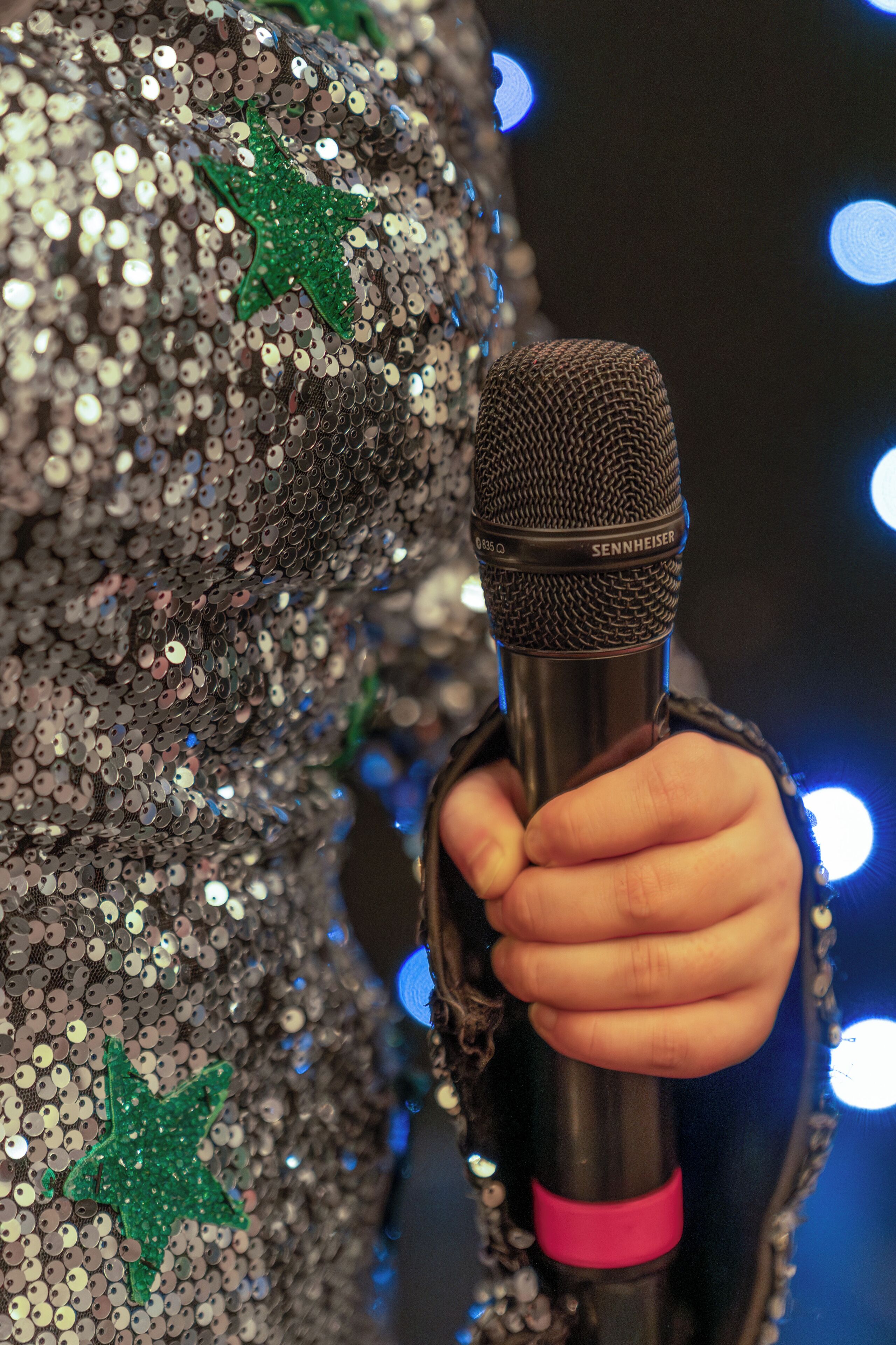 A hand holding a microphone with a sequined garment in the background.