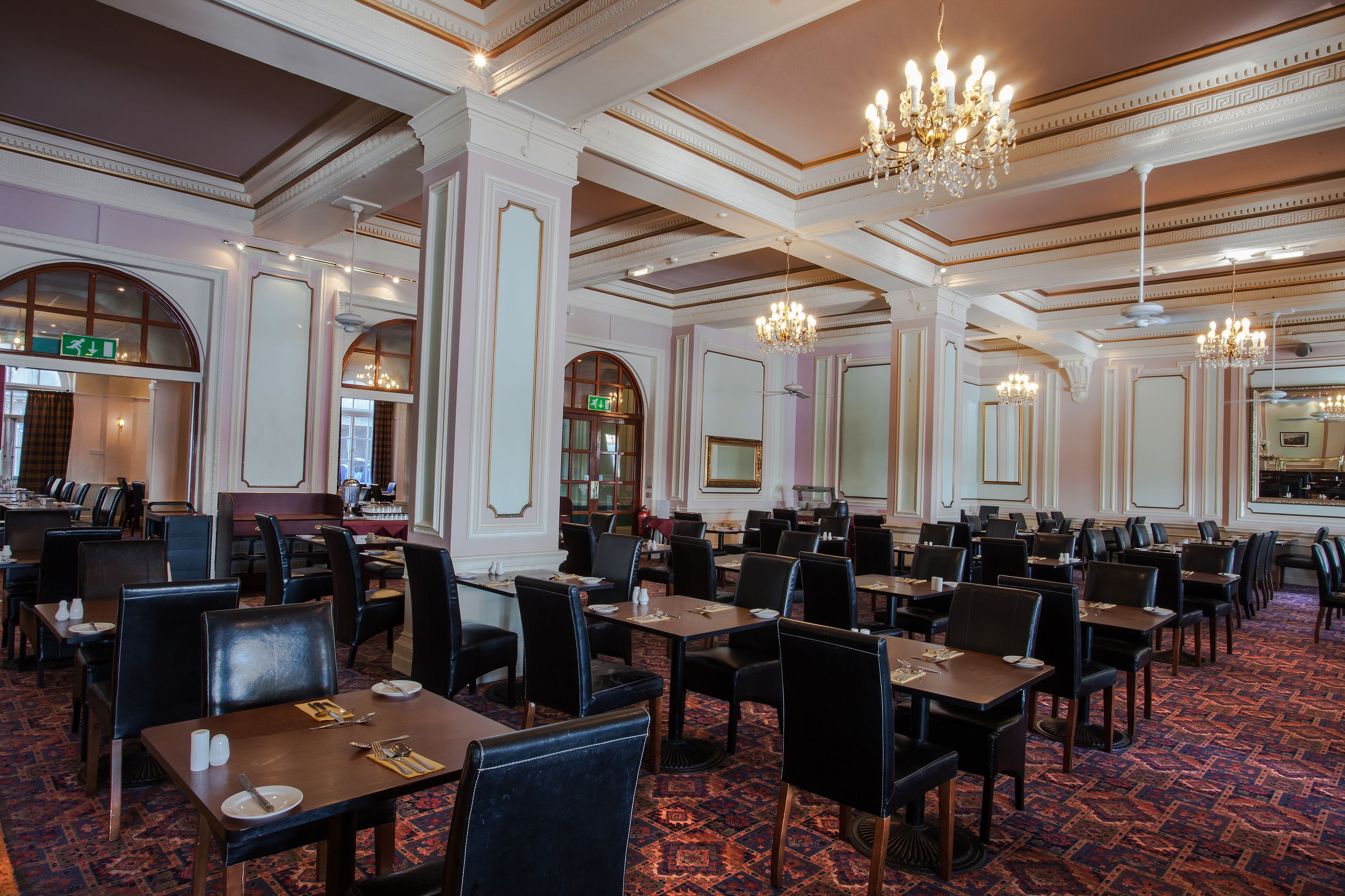 A spacious dining area with multiple tables and chairs, elegant chandeliers, and a patterned carpet.