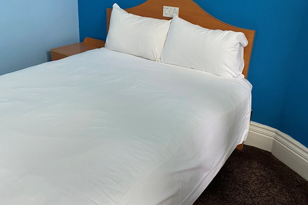 Un lit bien fait, avec du linge de lit blanc, dans une pièce aux murs bleus et dotée d’une tête de lit en bois.
