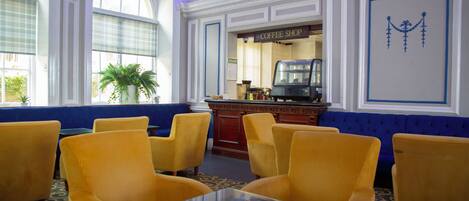 A room with yellow upholstered chairs, a coffee shop sign, and a large window with a plant.